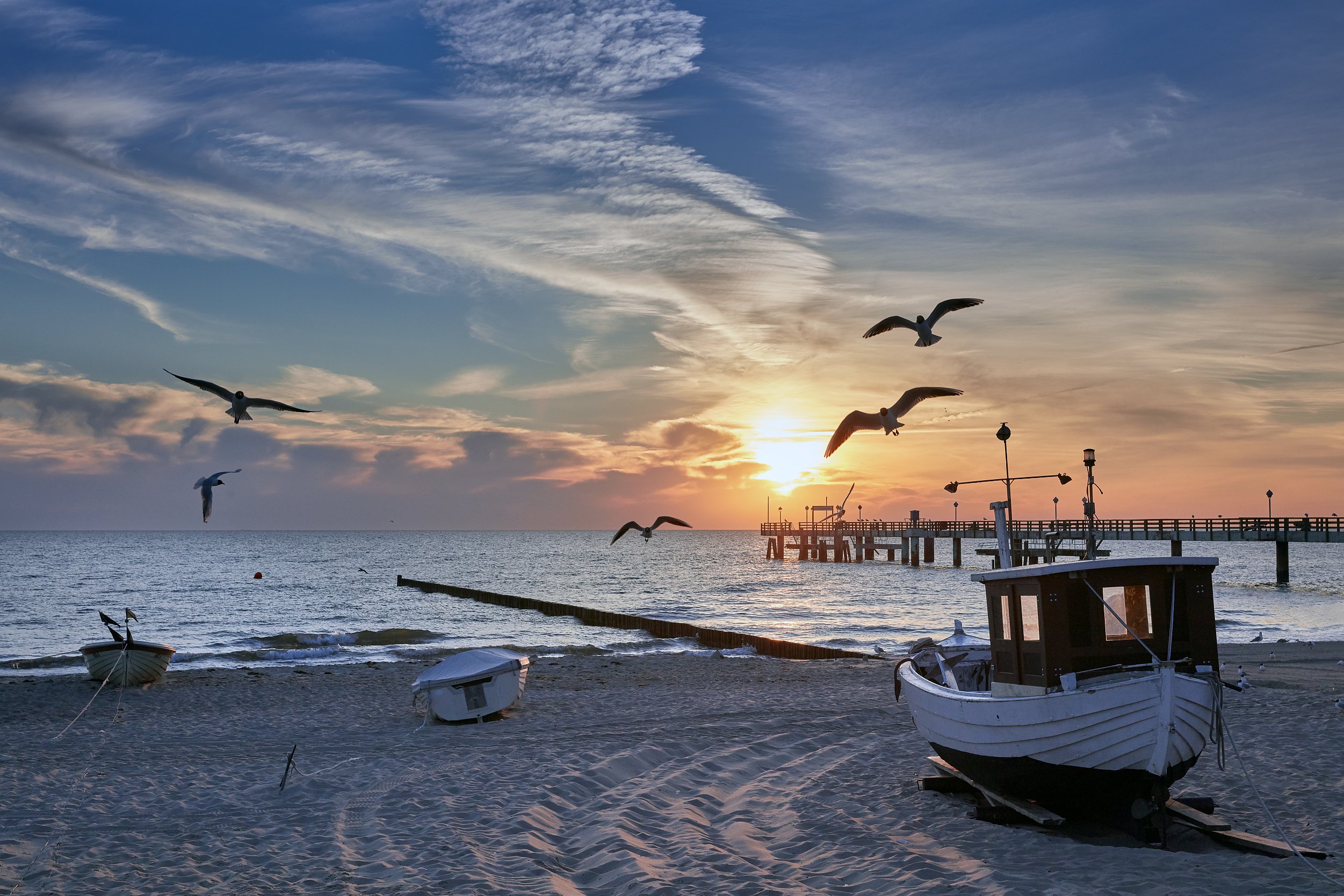 Strand von Koserow in der Abendsonne. Am Himmel fliegen 5 Möwen, im Sand liegen drei kleine Boote.